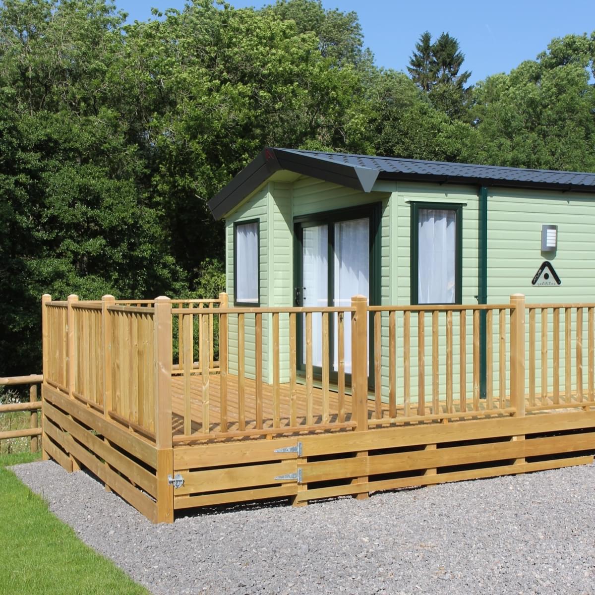 a holiday home with a timber wraparound balcony with trees in the background and a pristine gravel parking spot next to it