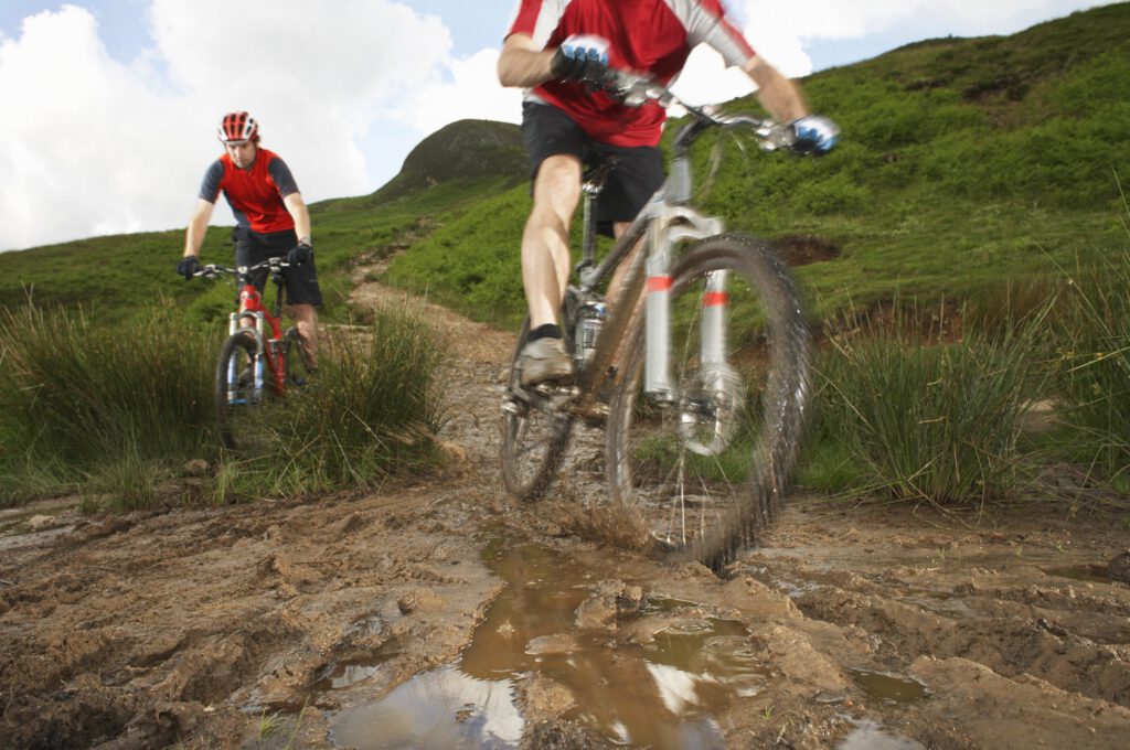 two cyclists on mountain bikes on muddy nature trail
