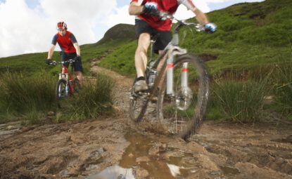 two cyclists on mountain bikes on muddy nature trail
