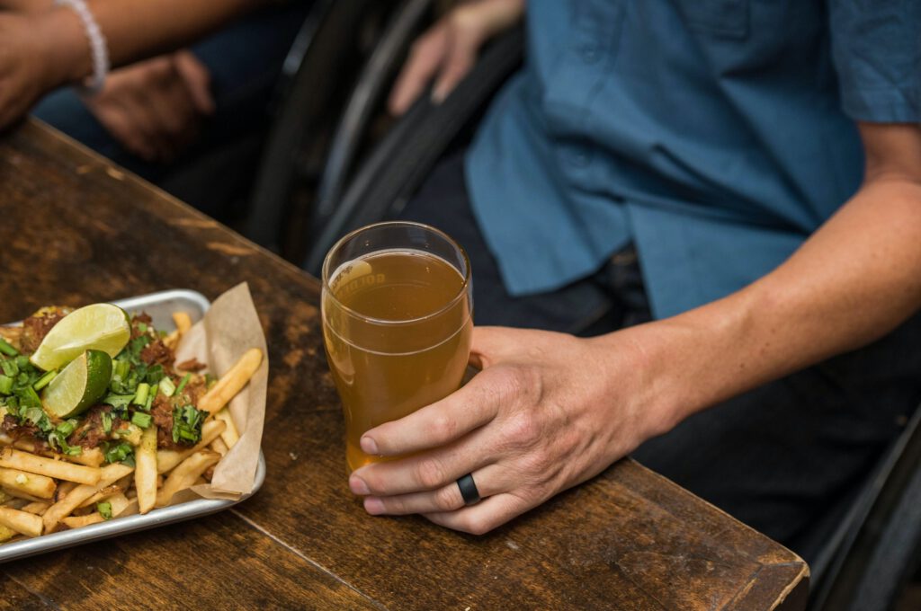 man holding pint of beer with food on the table