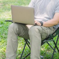 man sitting in camping chair outside on his laptop