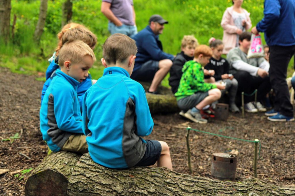 group of childrens sitting on logs in woodland learning bushcraft skills