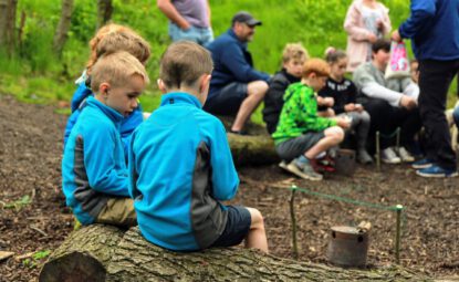 group of childrens sitting on logs in woodland learning bushcraft skills