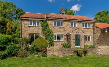 two story stone built house with pretty garden and surrounded by trees