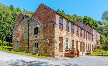 old converted linen mill surrounded by trees on a sunny day