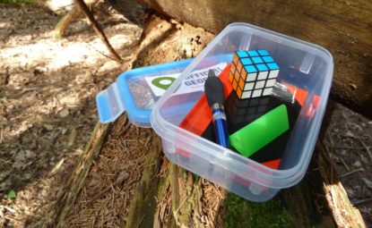 Tupperware box filled with small trinkets sitting open on log in woodland