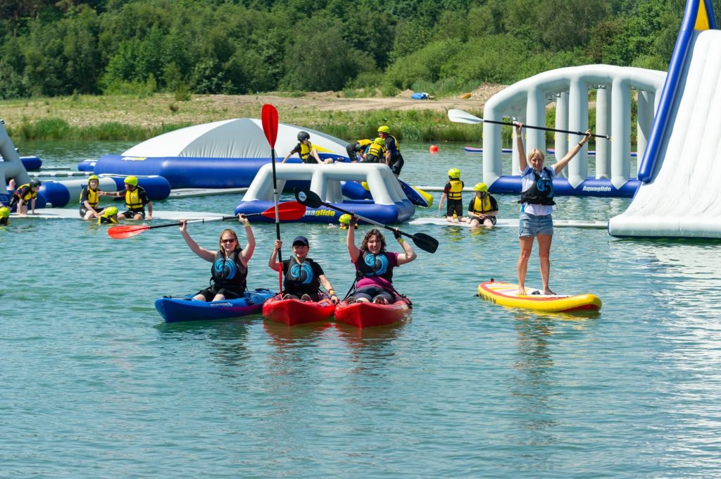 Huge inflatable obstacle course in middle of lake, with people canoing and paddle boarding nearby