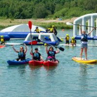 Huge inflatable obstacle course in middle of lake, with people canoing and paddle boarding nearby